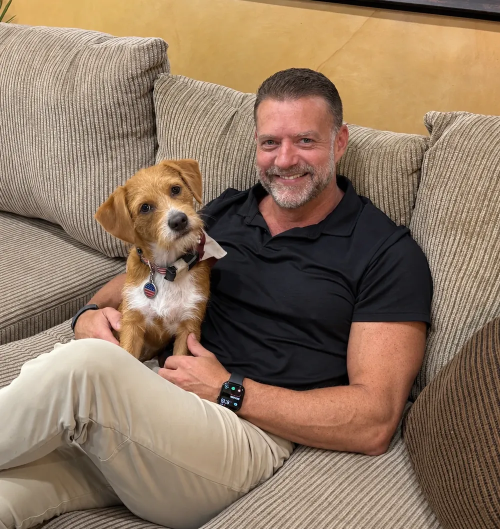 Dr. Steve Pelton on the couch at Hearthstone Animal Clinic with a scruffy terrier puppy in his lap